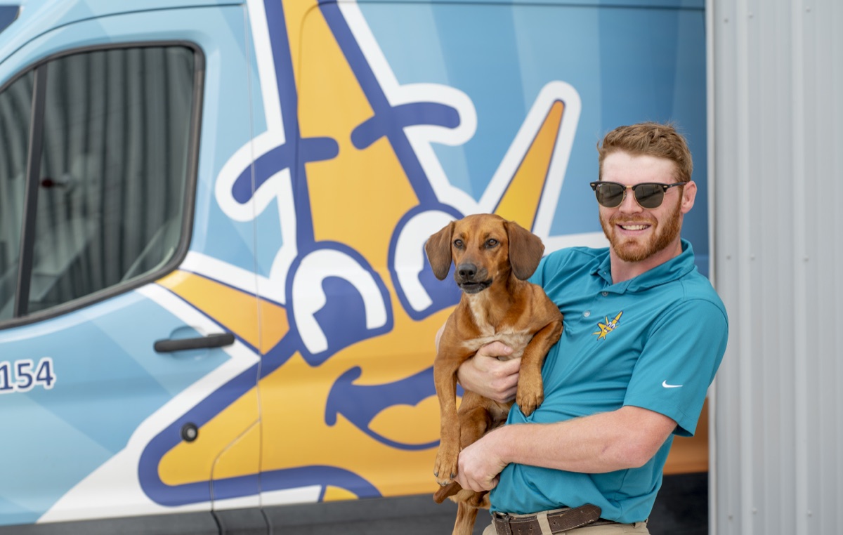 A True Comfort technician holding the shop dog in front of a service van